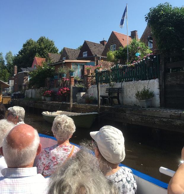 Menschen auf einem Boot blicken auf Häuser am Kanal.