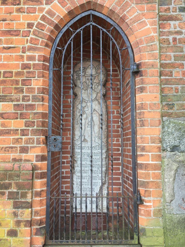 Nische mit Gitter und alter Statue in Backsteinwand.