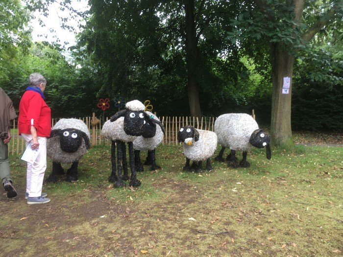 Gruppe steht bei Schaffiguren auf einer Wiese.